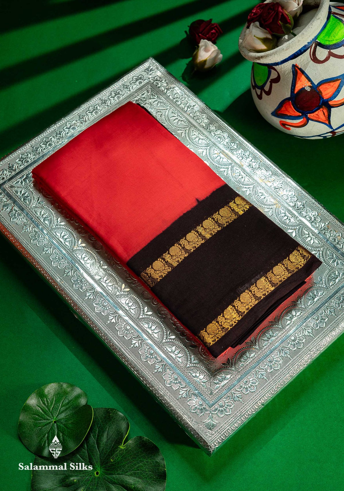 Red and black saree with gold border on a decorative tray against a green background Traditional Rettapet Border